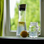 Una persona beve un bicchiere d'acqua al mattino, simboleggiando l'importanza dell'idratazione.